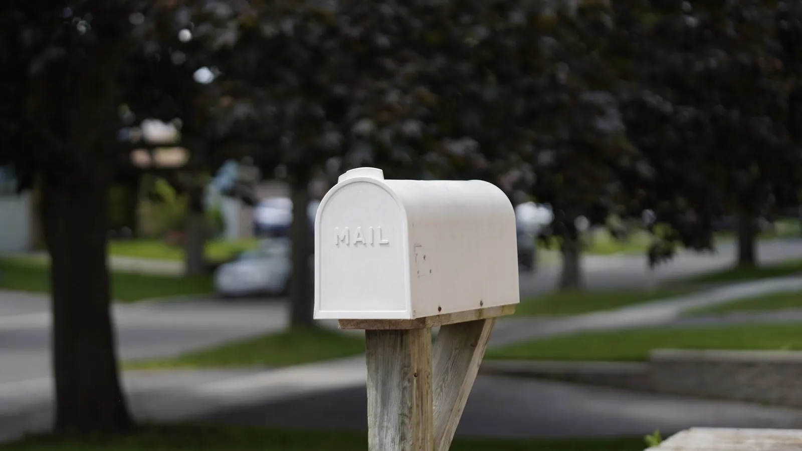 A classic white residential mailbox on a wooden post at the curb