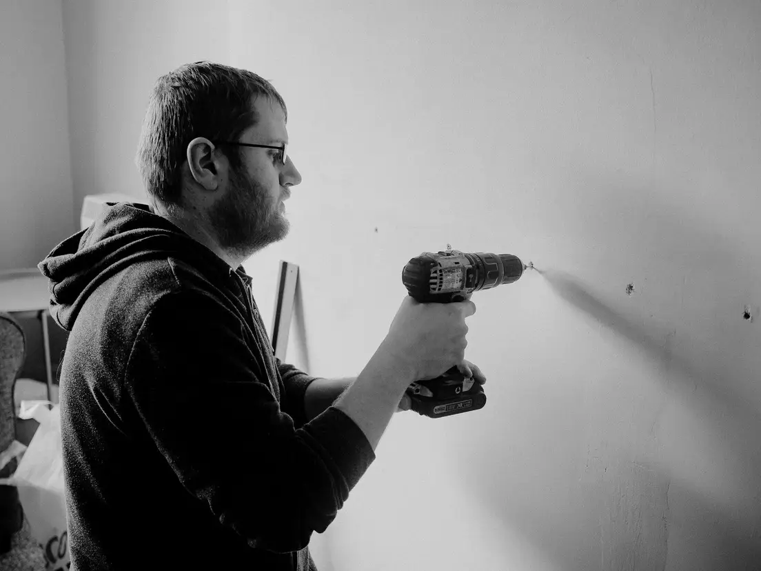 A person using a stud finder against a wall to locate ceiling joists before framing a temporary wall