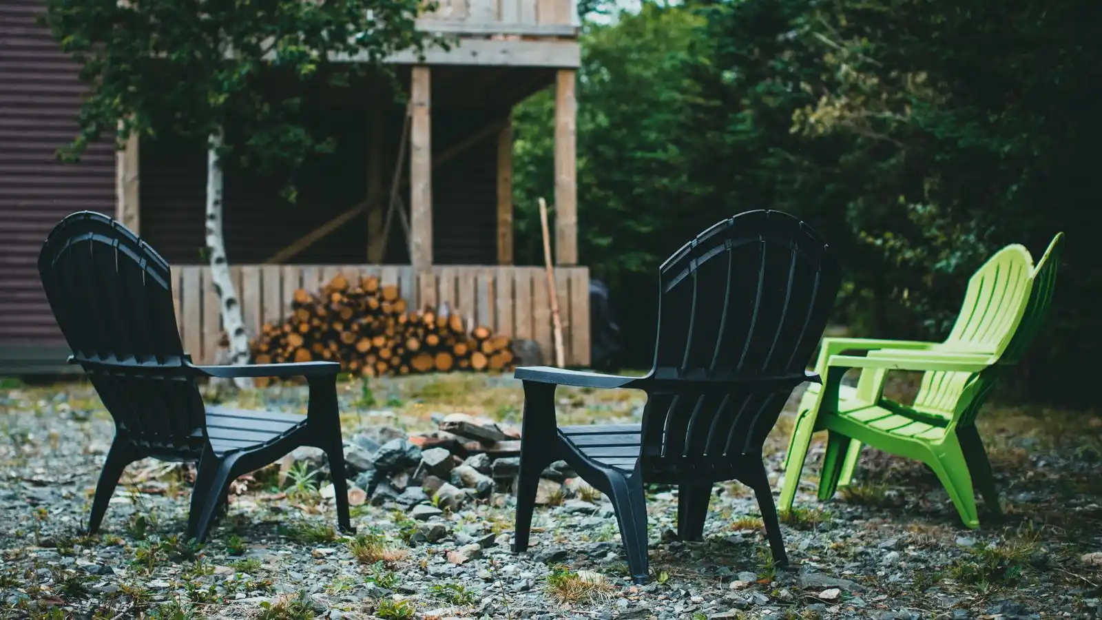 Three resin Adirondack chairs, one lime green, around a fire pit on a gravel backyard pad