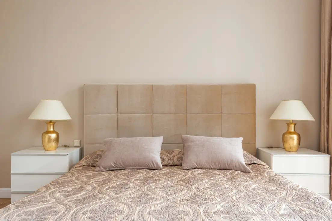 Matching white nightstands with identical gold table lamps on both sides of a bed with an upholstered headboard