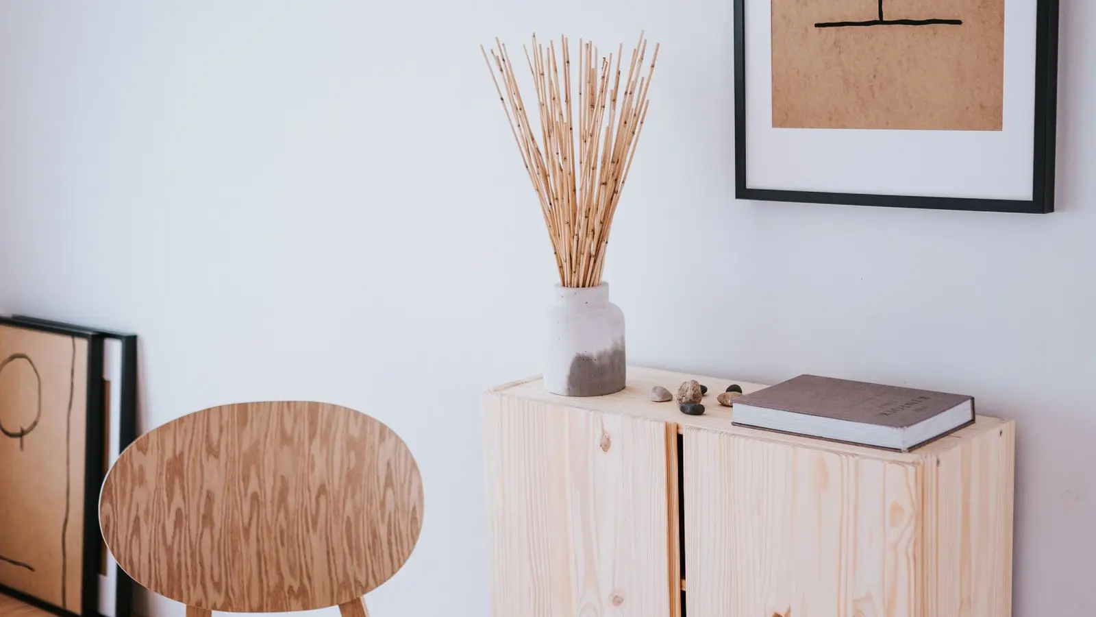 Close-up of a light plywood chair, pine cabinet, and dried grass vase showing mixed natural wood tones