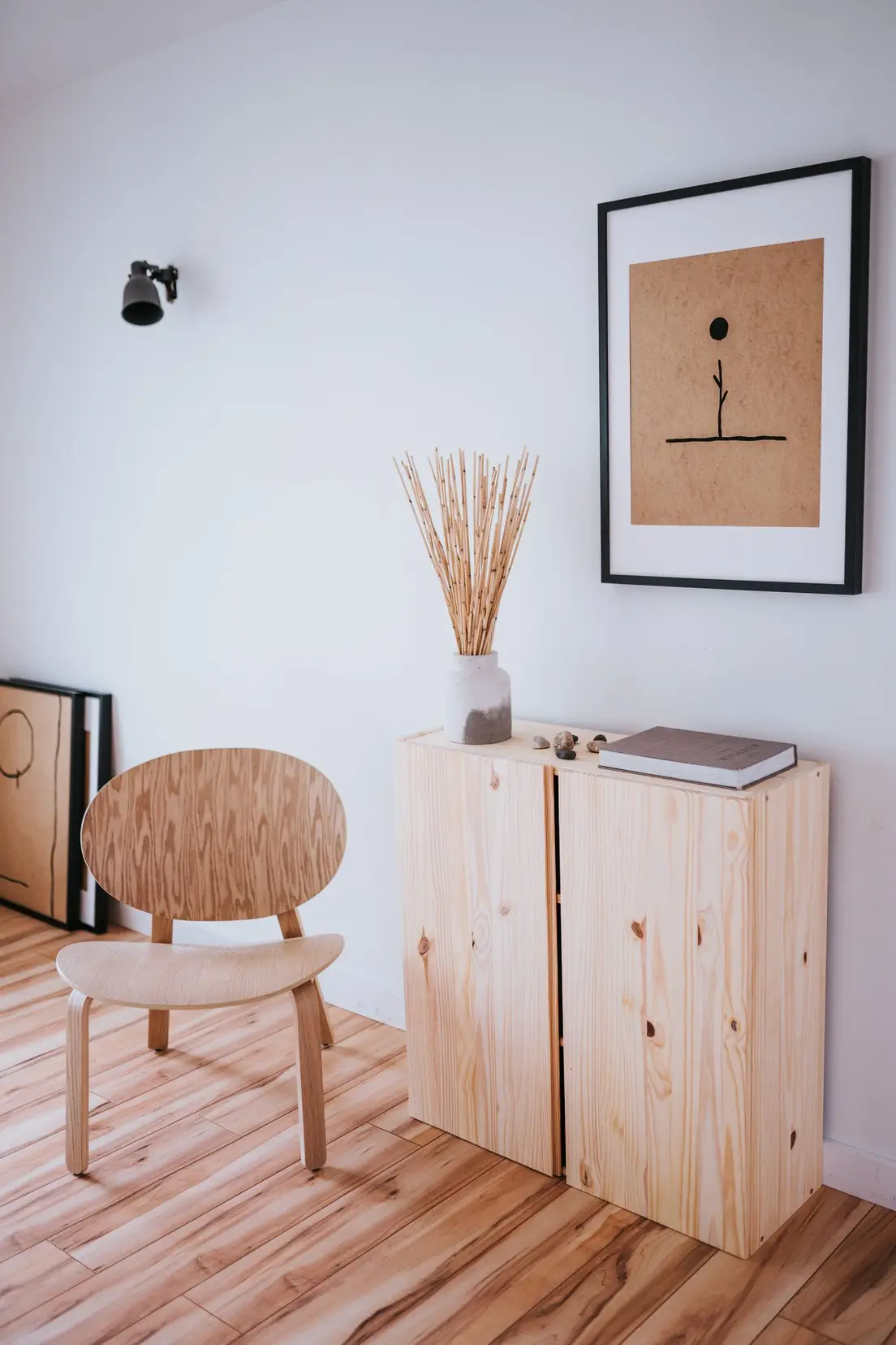 Close-up of a light plywood chair, pine cabinet, and dried grass vase showing mixed natural wood tones