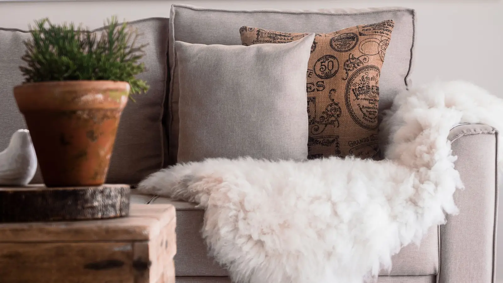 A terracotta planter, linen throw pillow, and sheepskin throw layered on a sofa