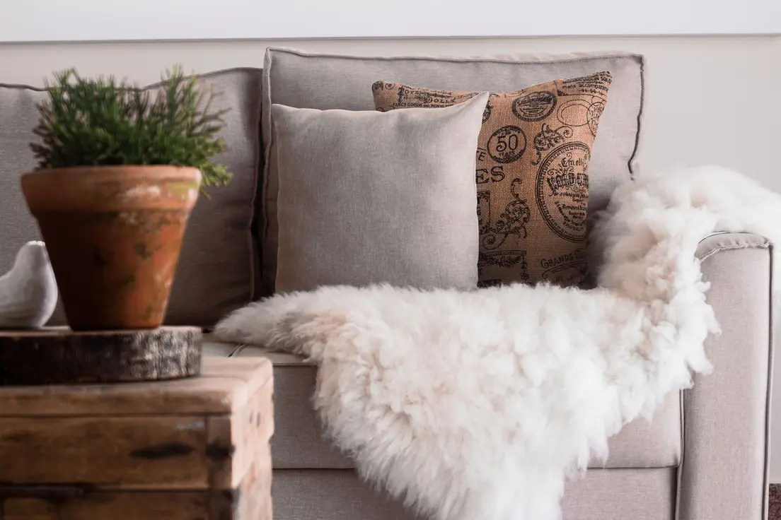 A terracotta planter, linen throw pillow, and sheepskin throw layered on a sofa
