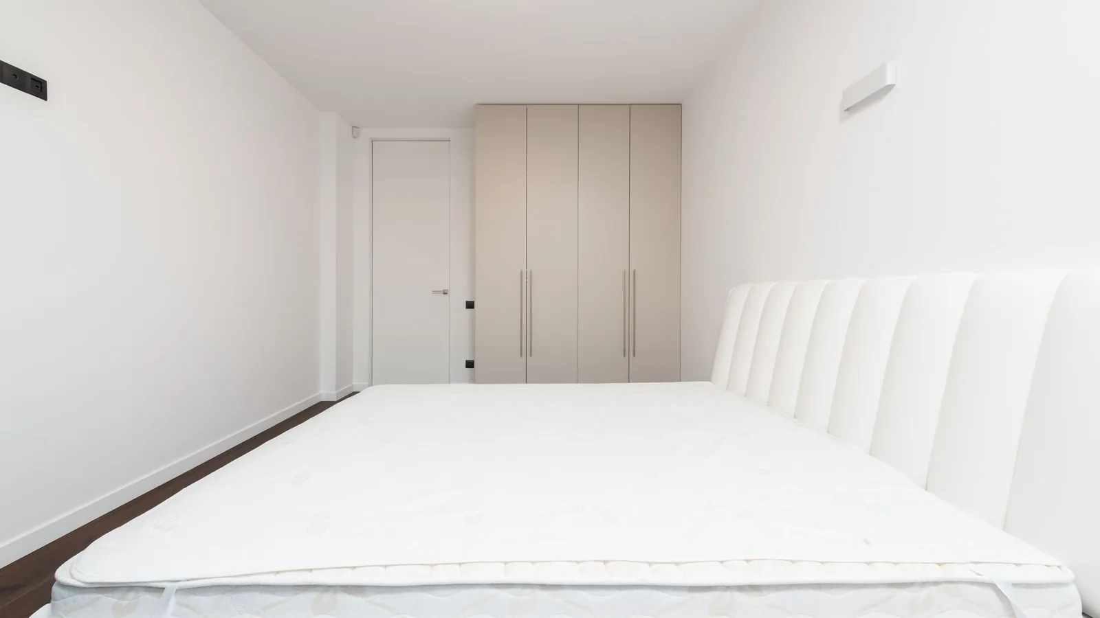A plain white mattress topper on a bed frame in a minimal bedroom