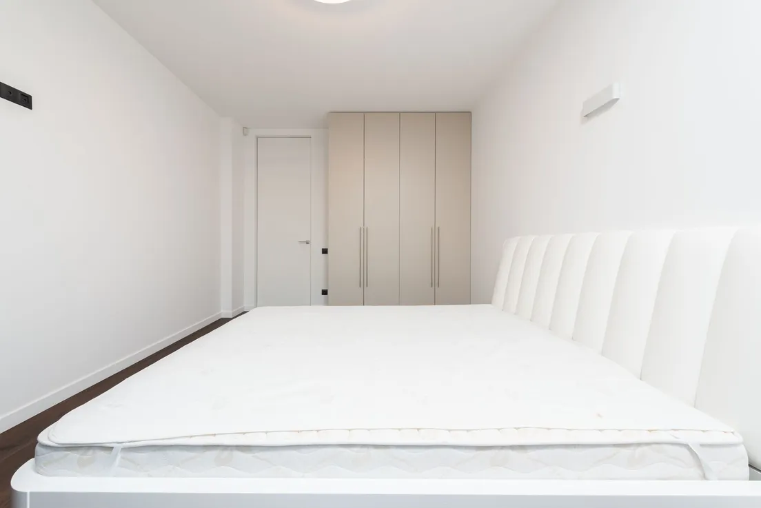 A plain white mattress topper on a bed frame in a minimal bedroom