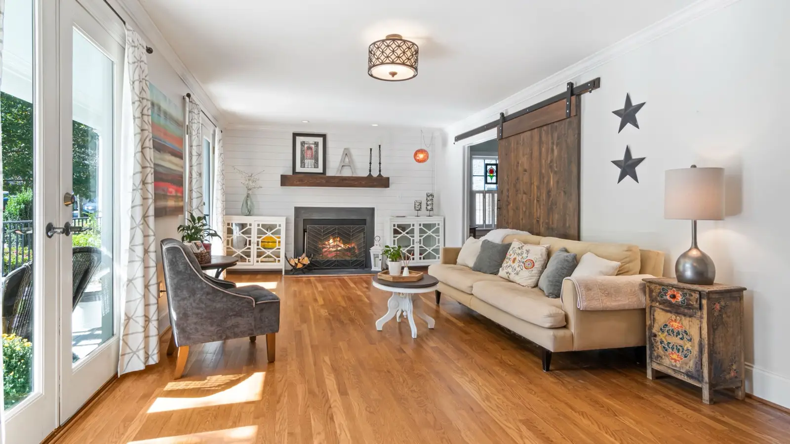 A modern farmhouse living room with a cream sofa, dark wood mantel, and star wall decor