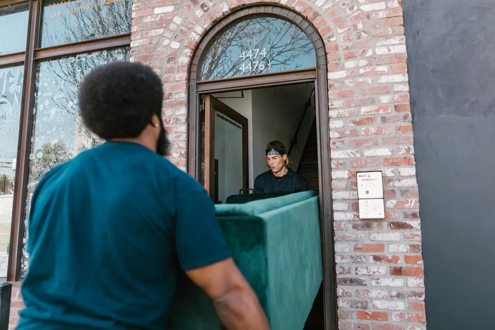 Two people carrying a green sofa through a narrow apartment doorway, the reason to measure before buying multifunctional furniture for a small apartment