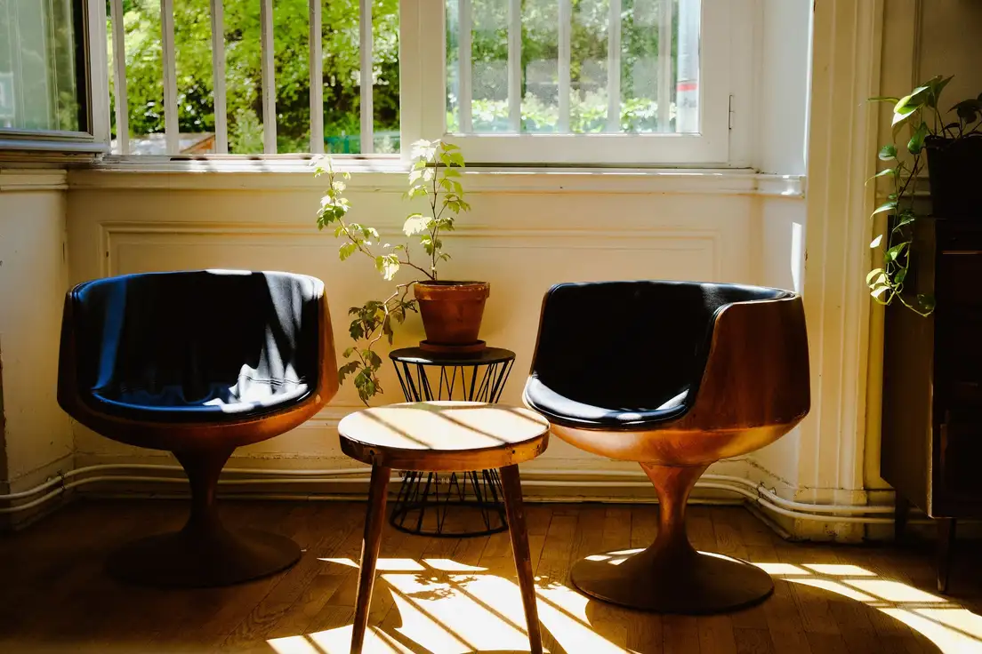 Two mid-century modern walnut tulip-base chairs with black leather seats beside a tapered-leg side table in a sunny room