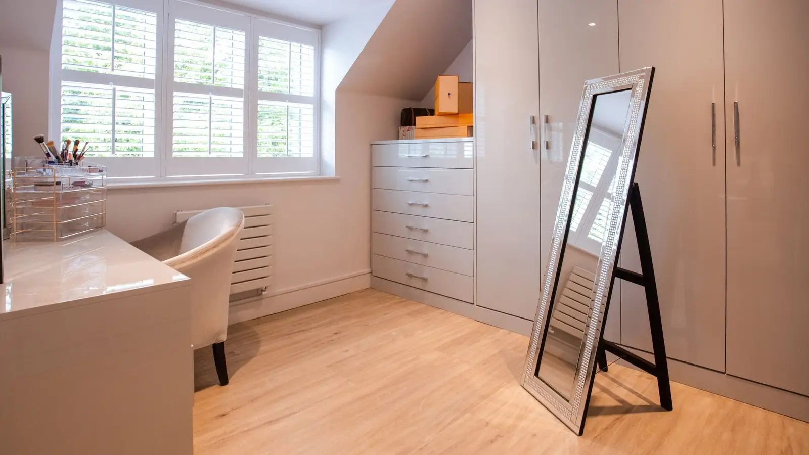 A leaning floor mirror beside a wardrobe and dresser in a small attic bedroom