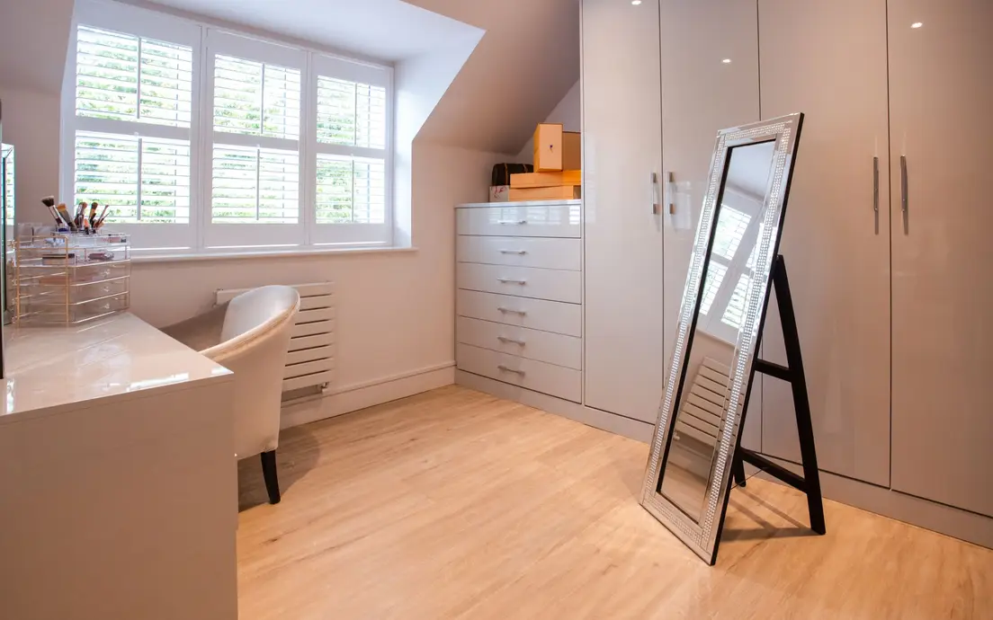 A leaning floor mirror beside a wardrobe and dresser in a small attic bedroom