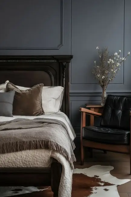 A bedroom with deep navy paneled walls, dark wood furniture, and warm lamp light, an example of a moody dark bedroom wall color