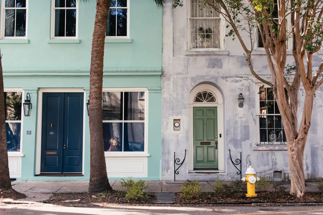 Two row houses with front doors painted navy and sage green against light blue and white facades