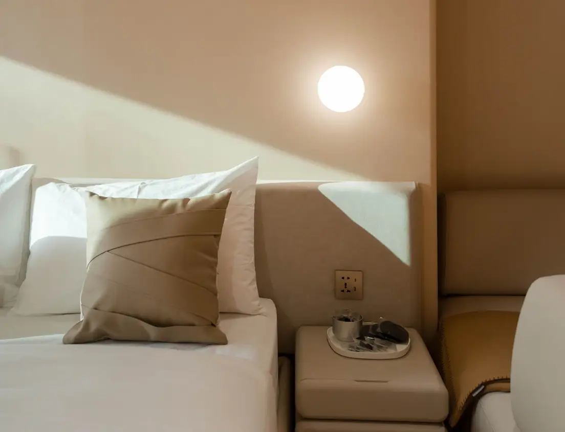 A bedside nightstand with a lamp plugged into a wall outlet in a small primary bedroom