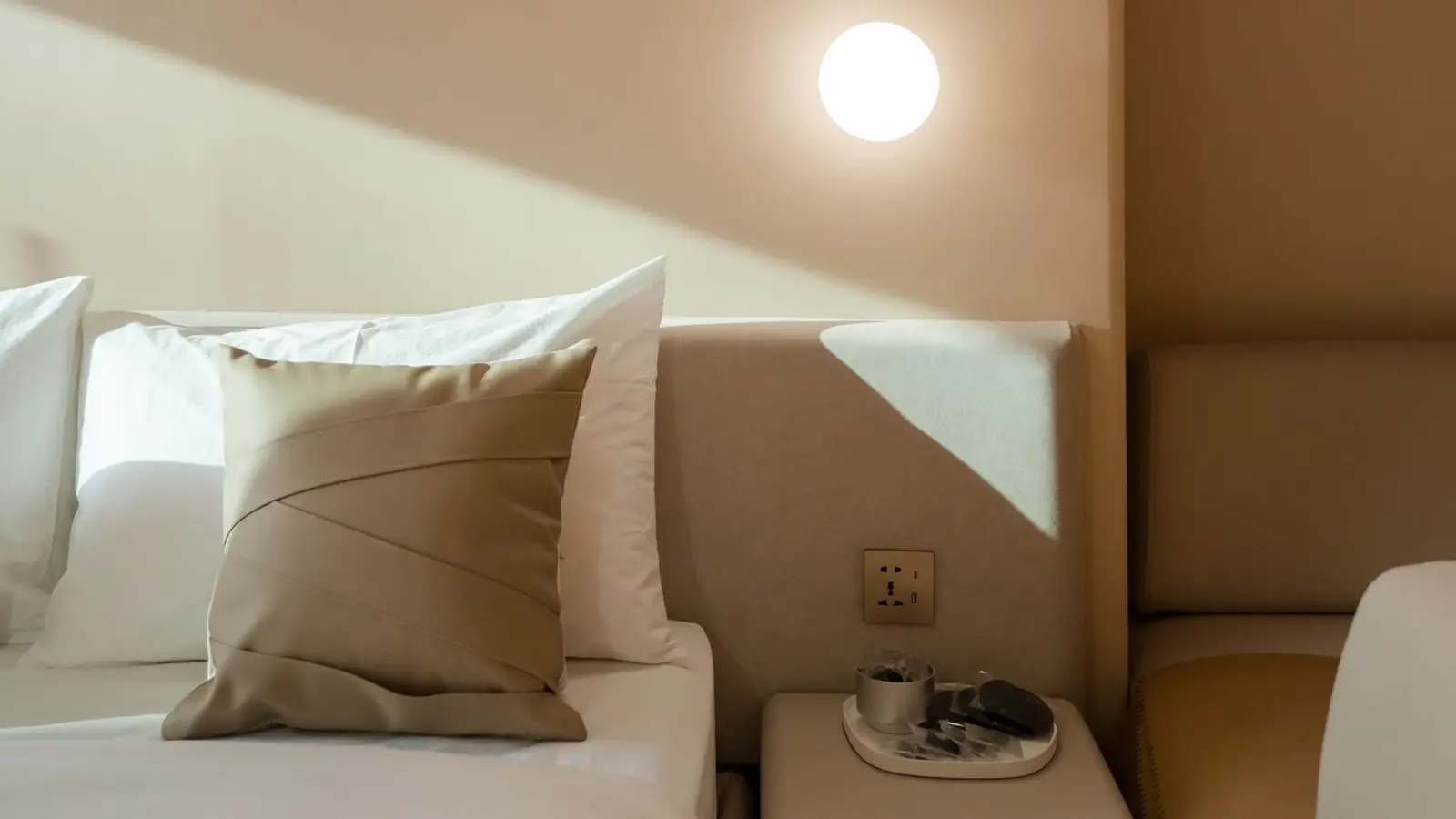 A bedside nightstand with a lamp plugged into a wall outlet in a small primary bedroom