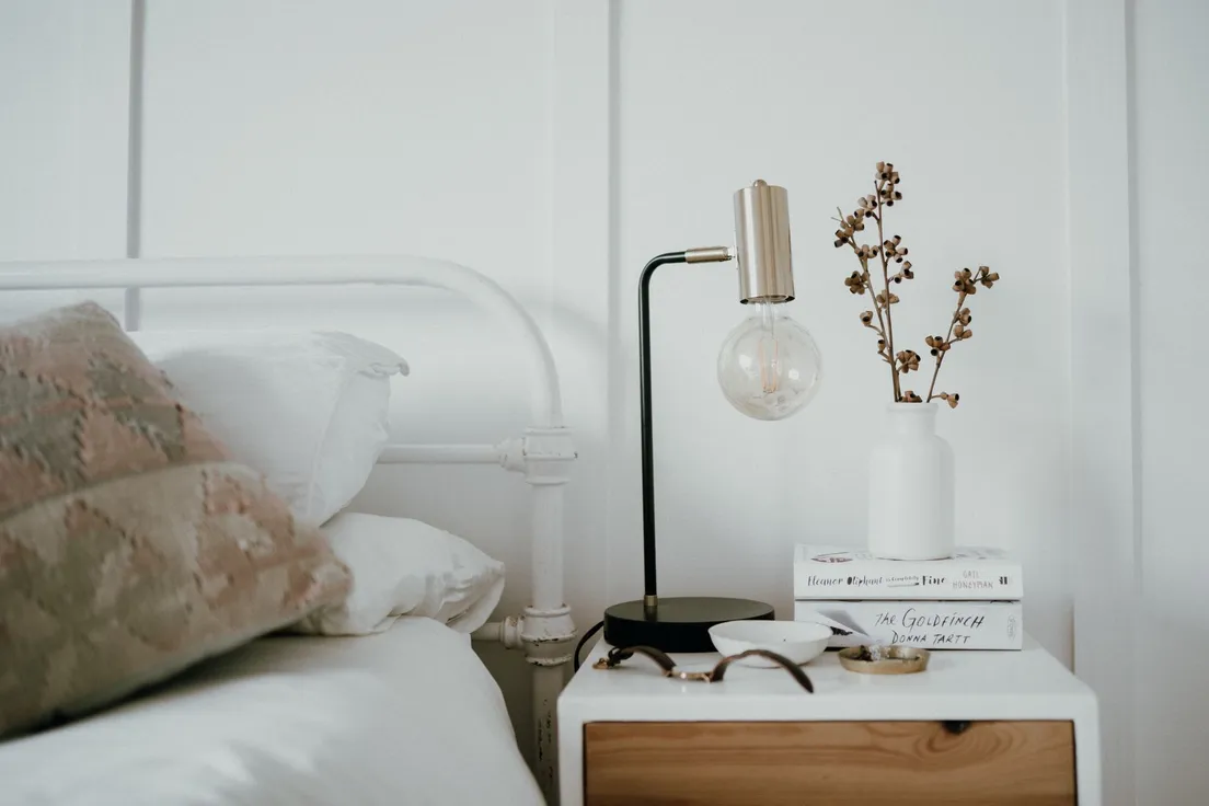 A styled nightstand with a lamp, a small vase, and a neat stack of books