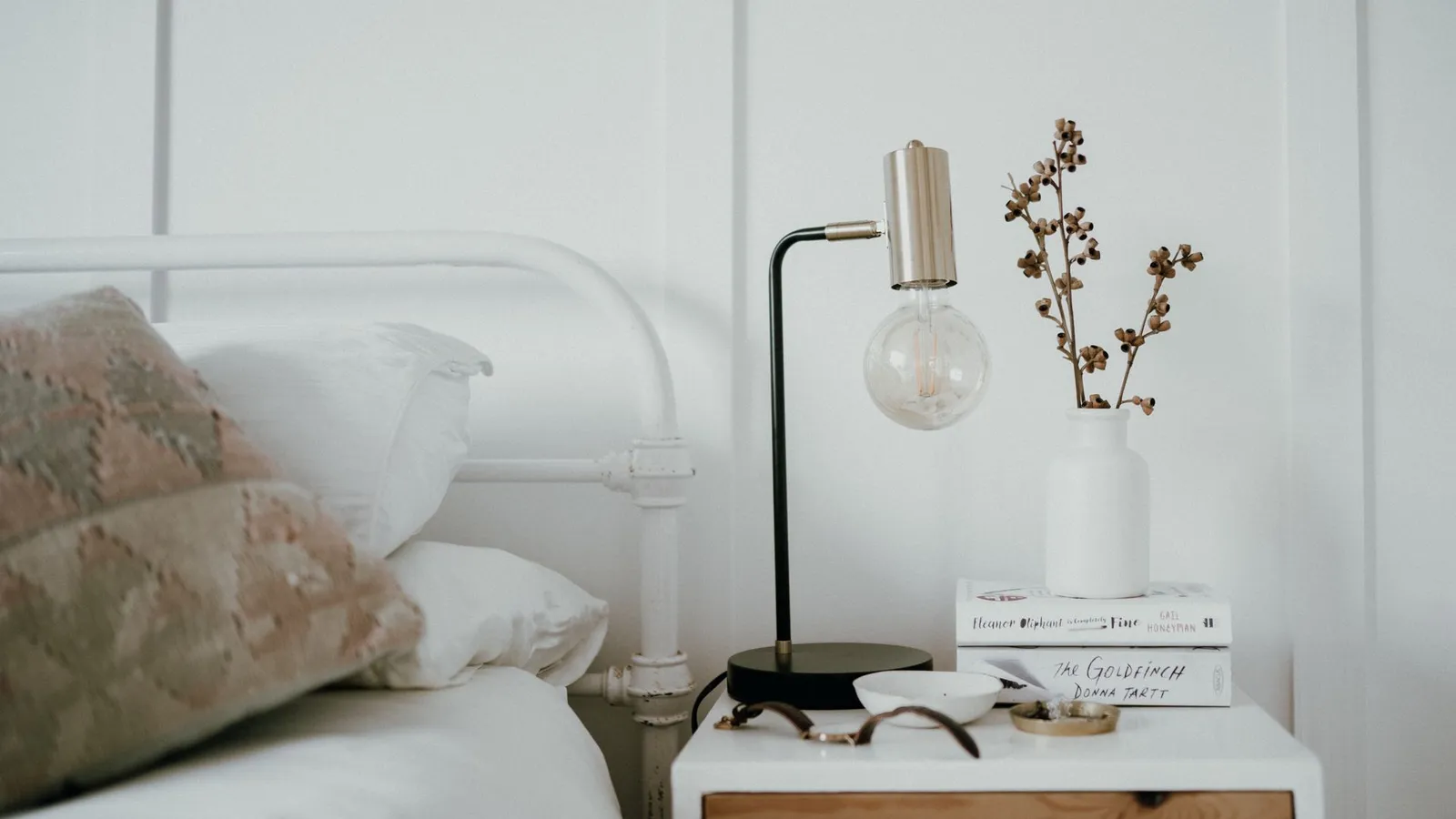 A styled nightstand with a lamp, a small vase, and a neat stack of books