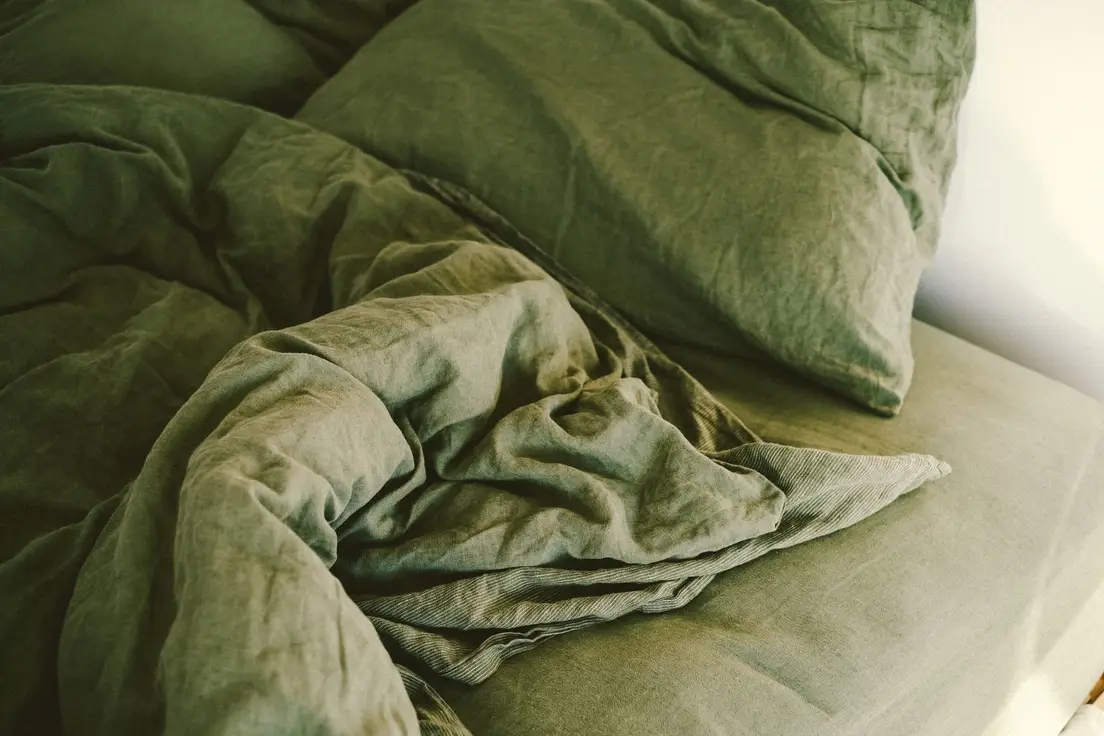 Rumpled olive linen bedding layered over a lighter sage sheet in a mens bedroom