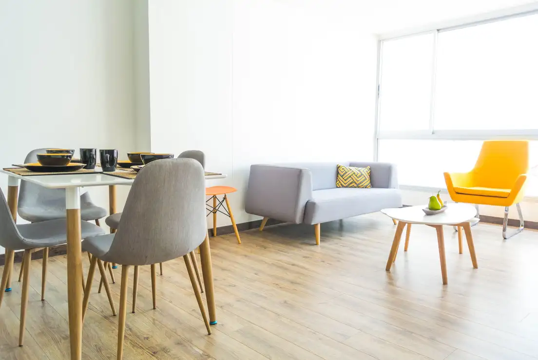 A small dining table with gray chairs beside an open walkway leading to a sofa, armchair, and coffee table in a bright living room dining room combo