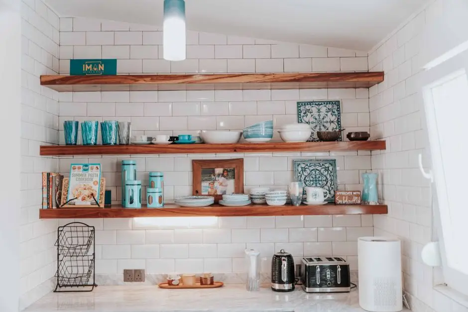 Open wood shelving styled with dishware and glassware against white subway tile in a kitchen