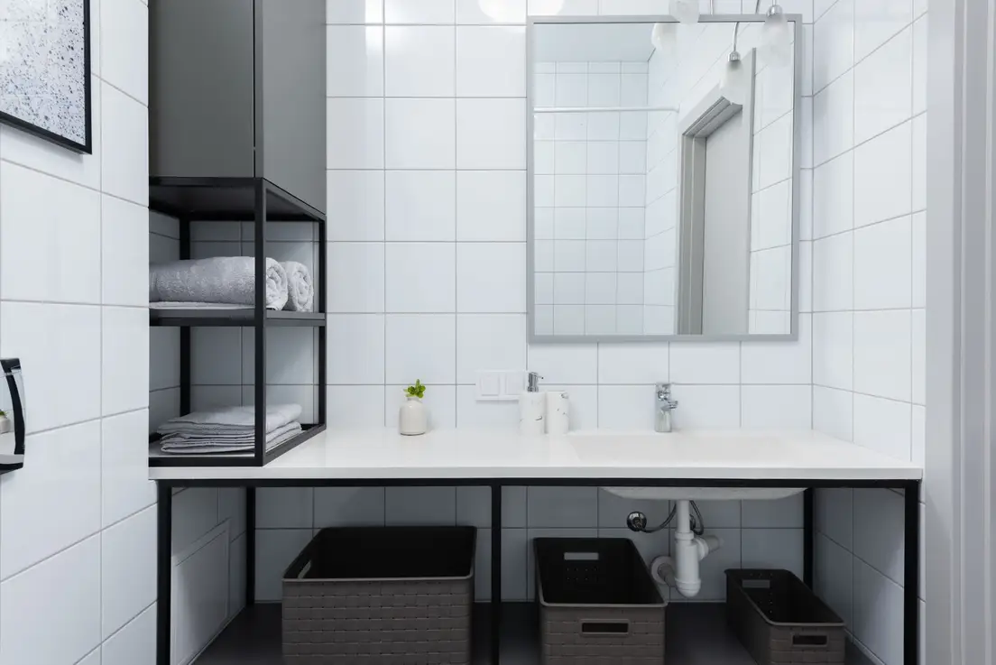 Black open wall shelving holding rolled towels above a small bathroom counter with storage baskets