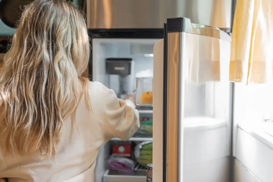 A woman reaching into an open refrigerator to organize food inside