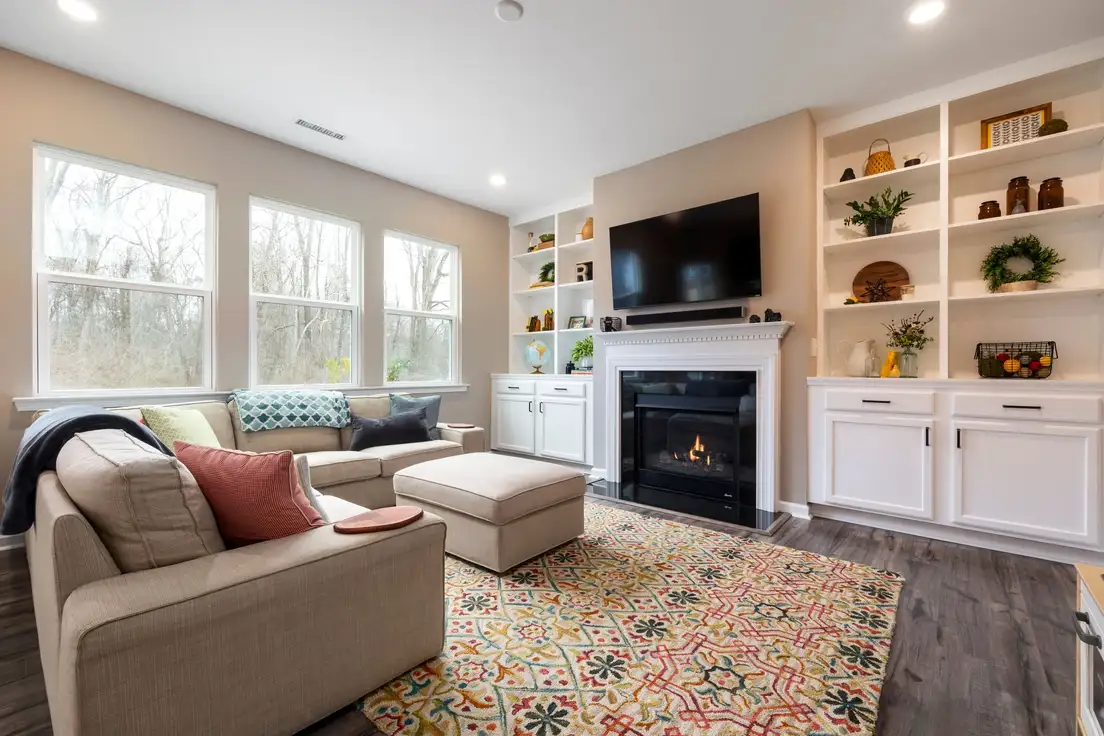 A beige sectional and matching ottoman facing a fireplace flanked by white built-in shelves with woven baskets in a family living room