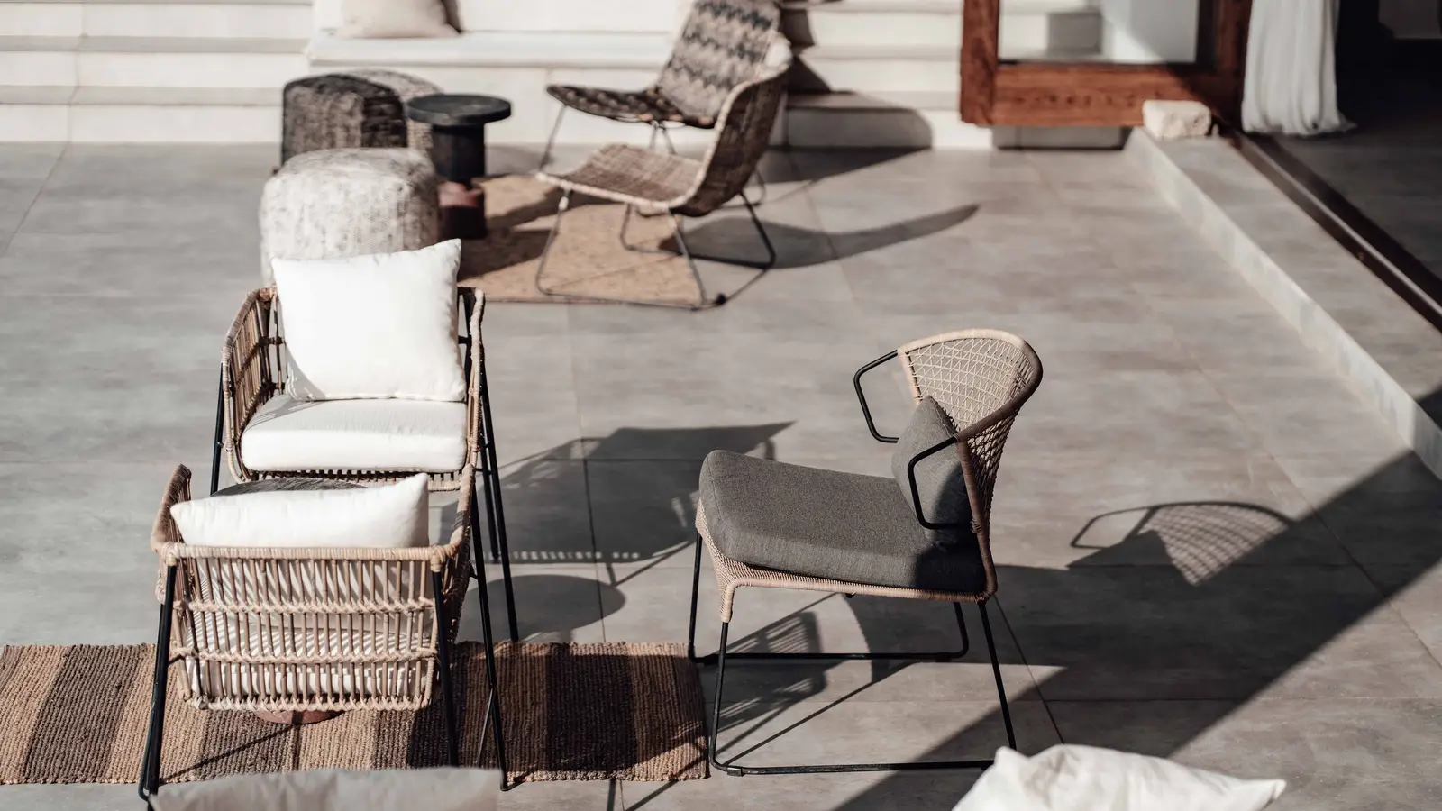 Rattan patio chairs layered with cushions and an outdoor rug