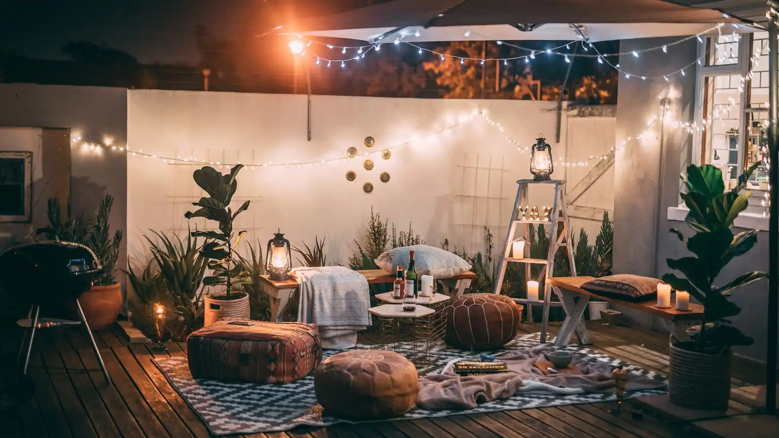 A geometric black-and-white outdoor rug defining a seating area with poufs and string lights on a deck at night