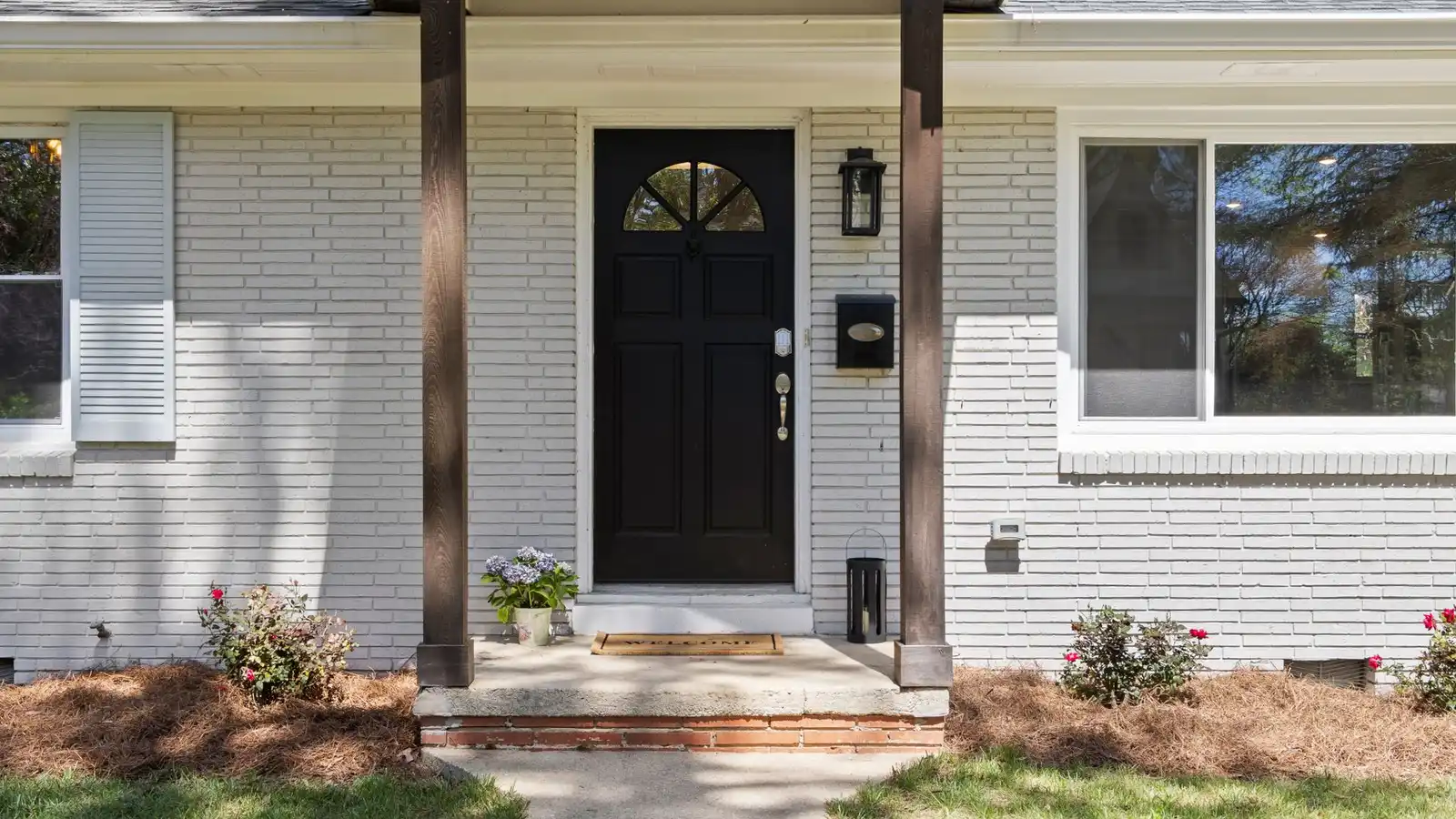 A ranch house entry with a small covered portico, wood columns, and a black front door