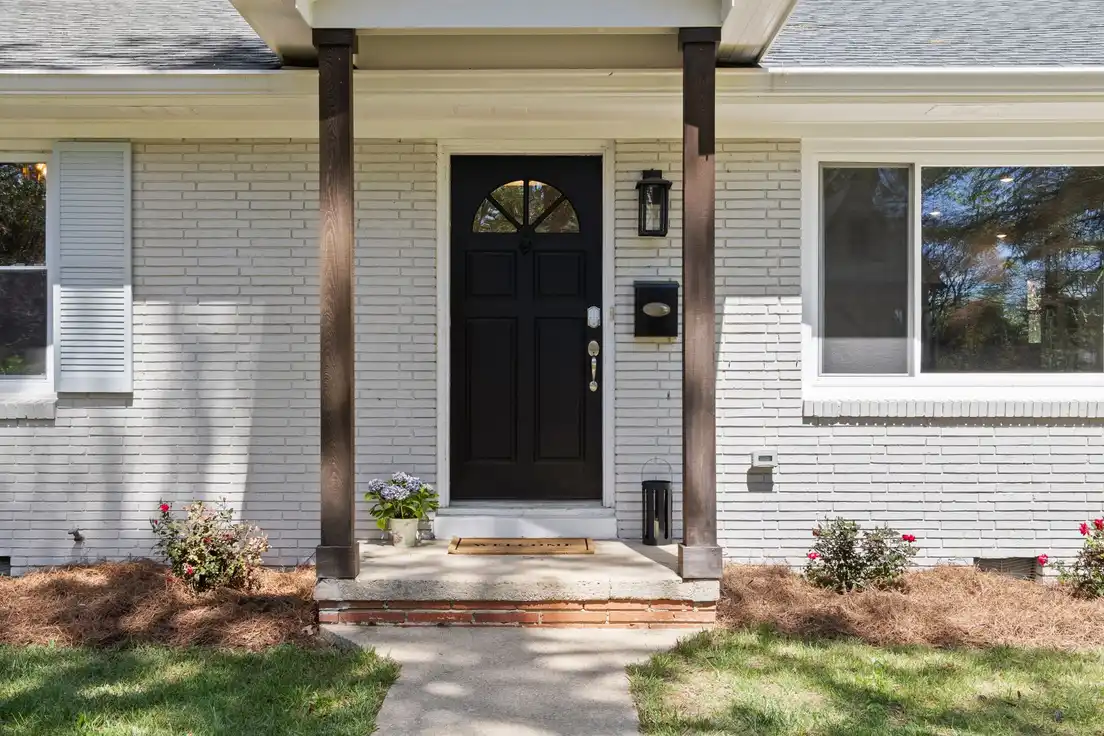 A ranch house entry with a small covered portico, wood columns, and a black front door
