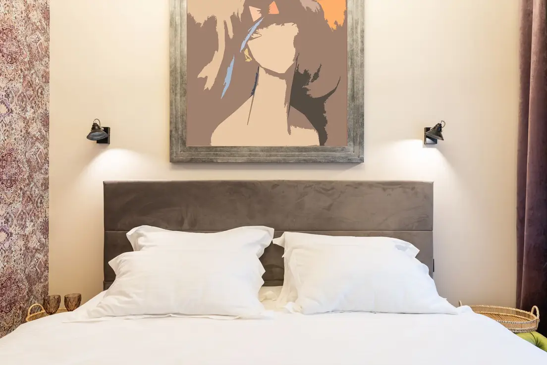 One oversized framed artwork hung above an upholstered bed between two black wall sconces