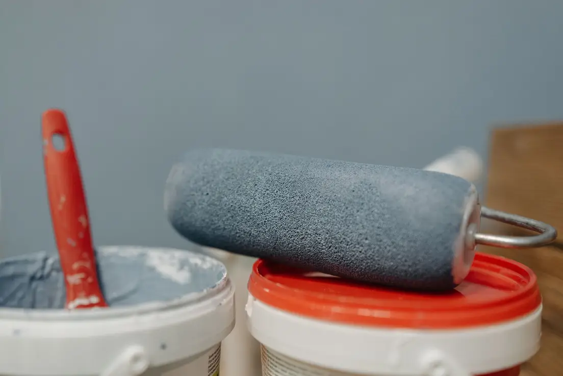 A paint roller resting on a tray beside a can of blue-grey wall paint