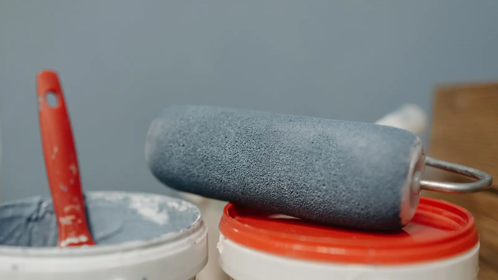 A paint roller resting on a tray beside a can of blue-grey wall paint