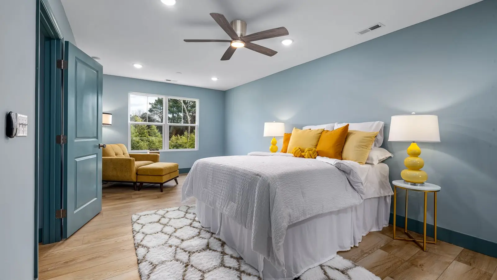 A bedroom with a bold blue accent wall and warm yellow bedding accents