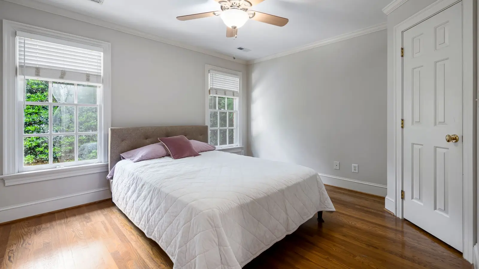 A small pale gray bedroom with matching wall and ceiling color and a wood ceiling fan