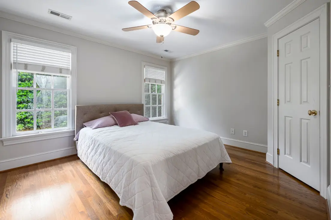 A small pale gray bedroom with matching wall and ceiling color and a wood ceiling fan