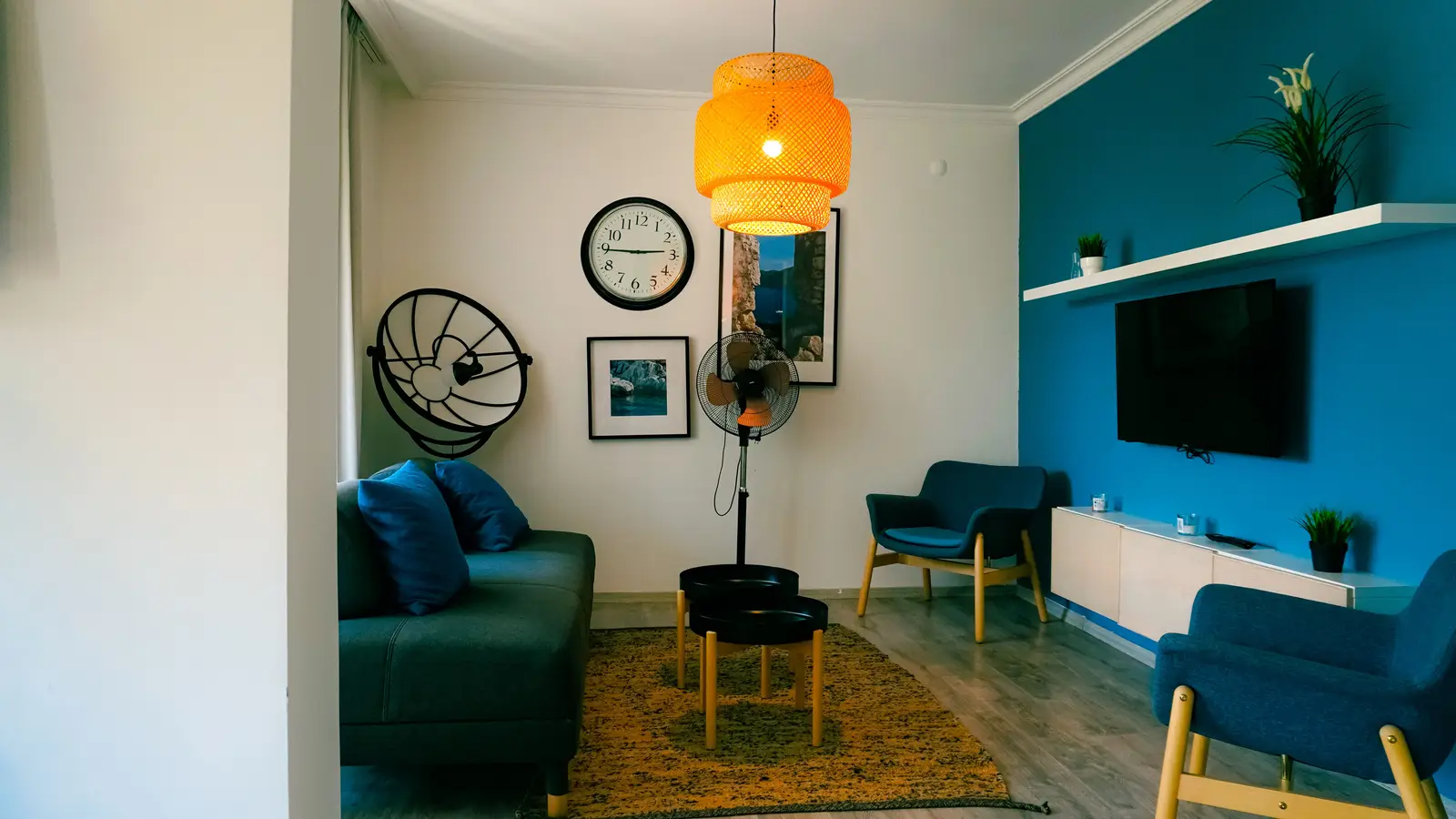 A bold blue accent wall behind a wall-mounted TV with a floating shelf above it