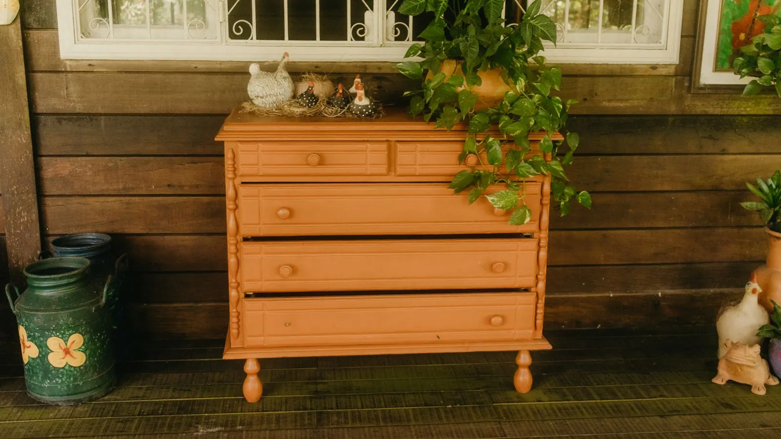 A thrifted wooden dresser painted bold terracotta orange, styled with a trailing plant