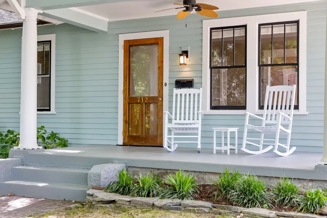 A small front porch with a freshly painted light gray floor and steps, two white rocking chairs, and a wood front door