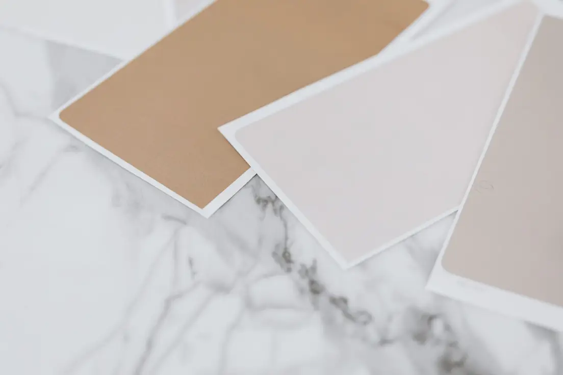 Warm neutral paint color swatches in tan, taupe, and dusty pink on a marble surface