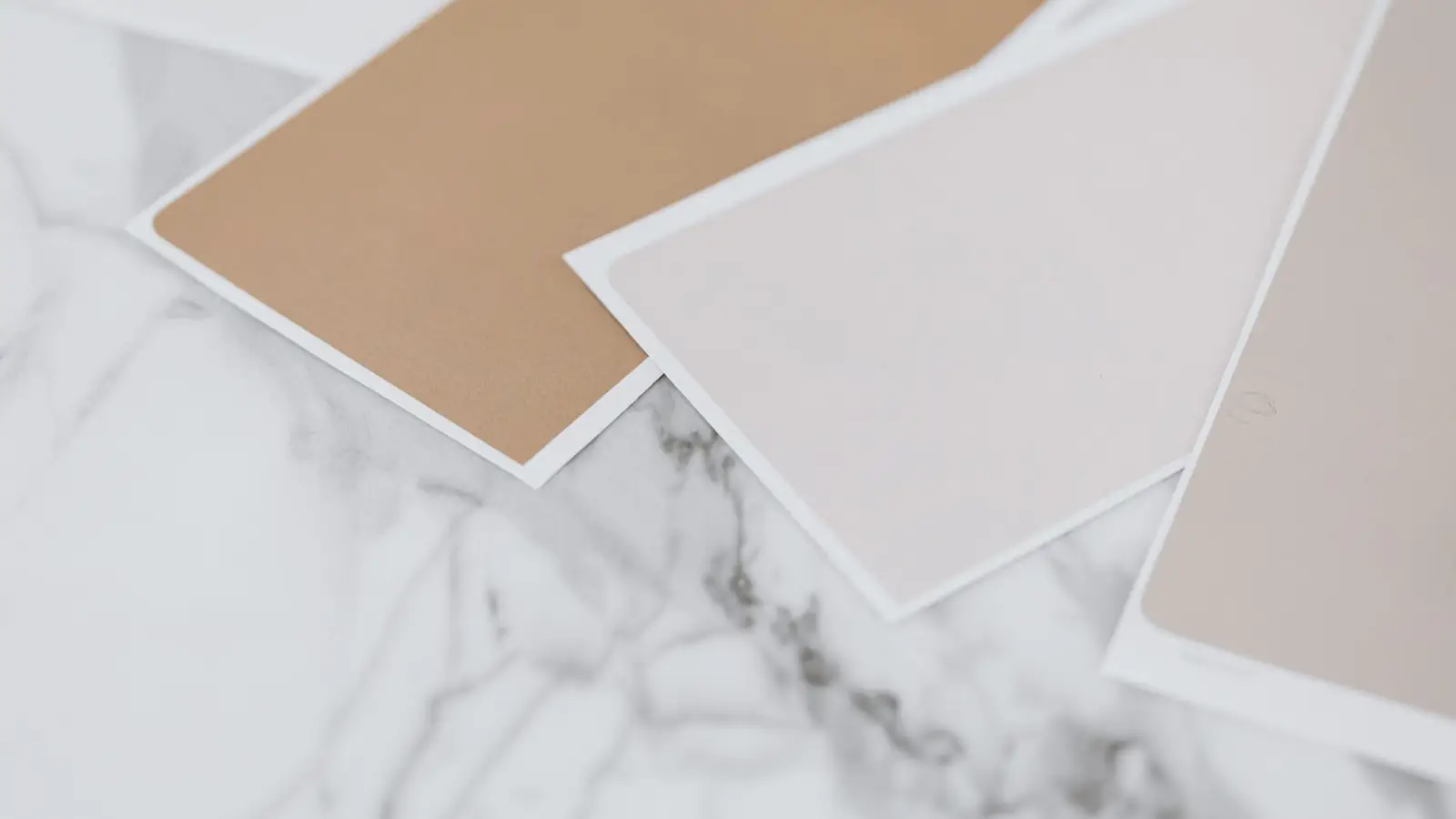 Warm neutral paint color swatches in tan, taupe, and dusty pink on a marble surface