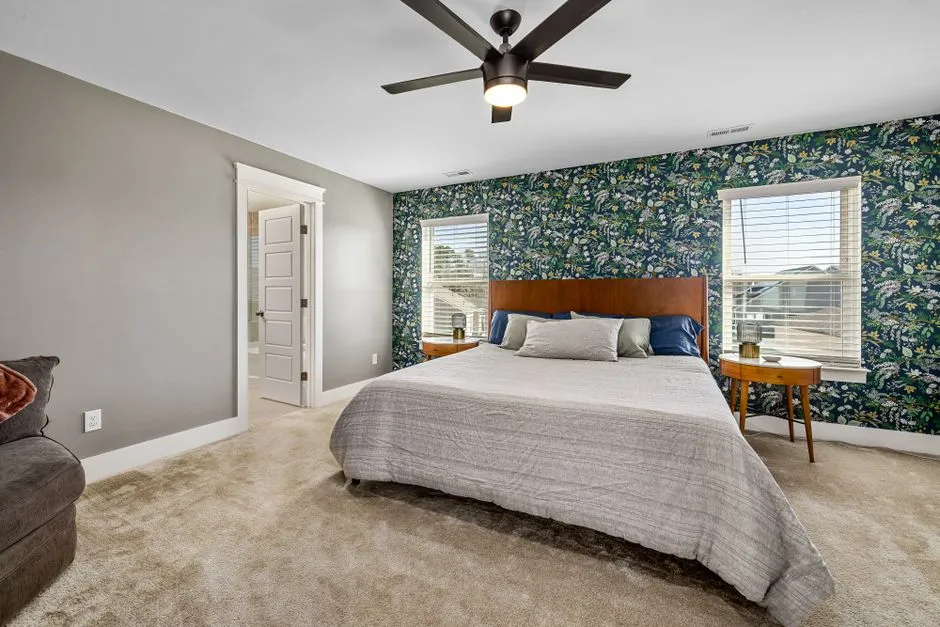 A bedroom with a bold floral accent wallpaper behind the headboard