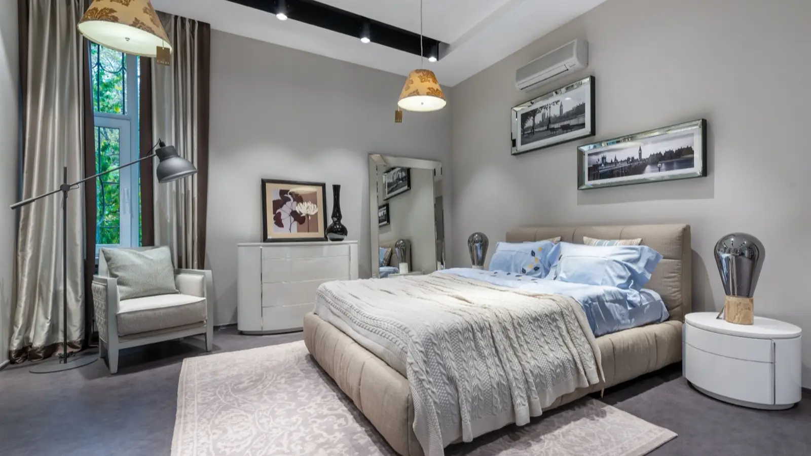 A patterned gray and cream area rug under a bed in a bedroom with framed art