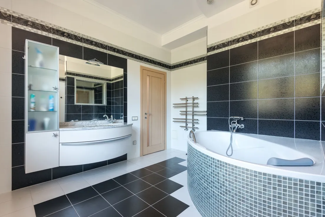 A bathroom with a black and white checkerboard tile floor, black patterned walls, and a mosaic-tiled tub