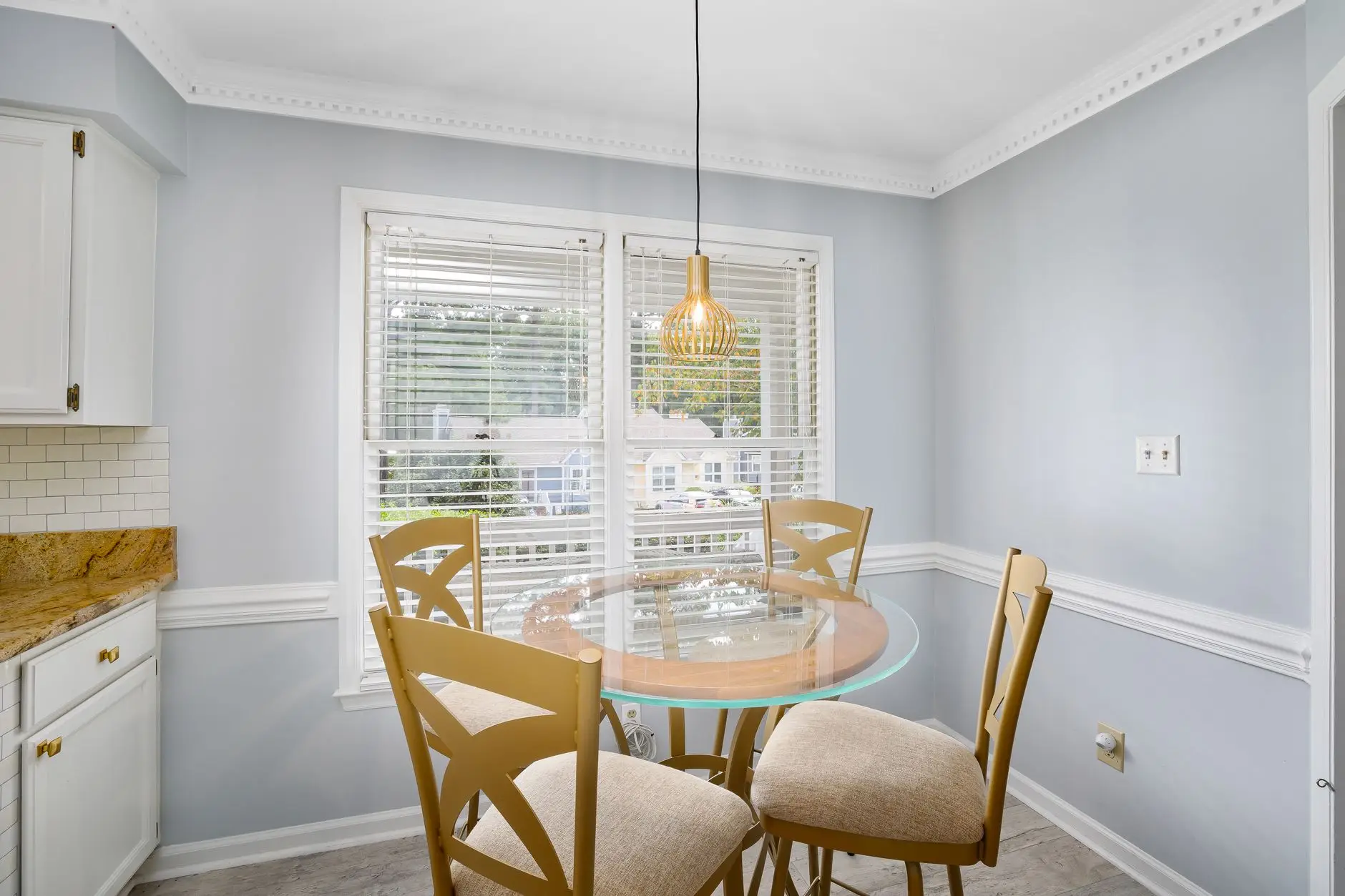 A glass-top pedestal dining table with wooden chairs in a small kitchen nook