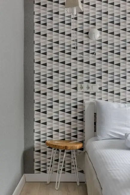 A bedroom corner with geometric peel-and-stick wallpaper behind a wooden stool, a renter-friendly alternative to painting bedroom walls