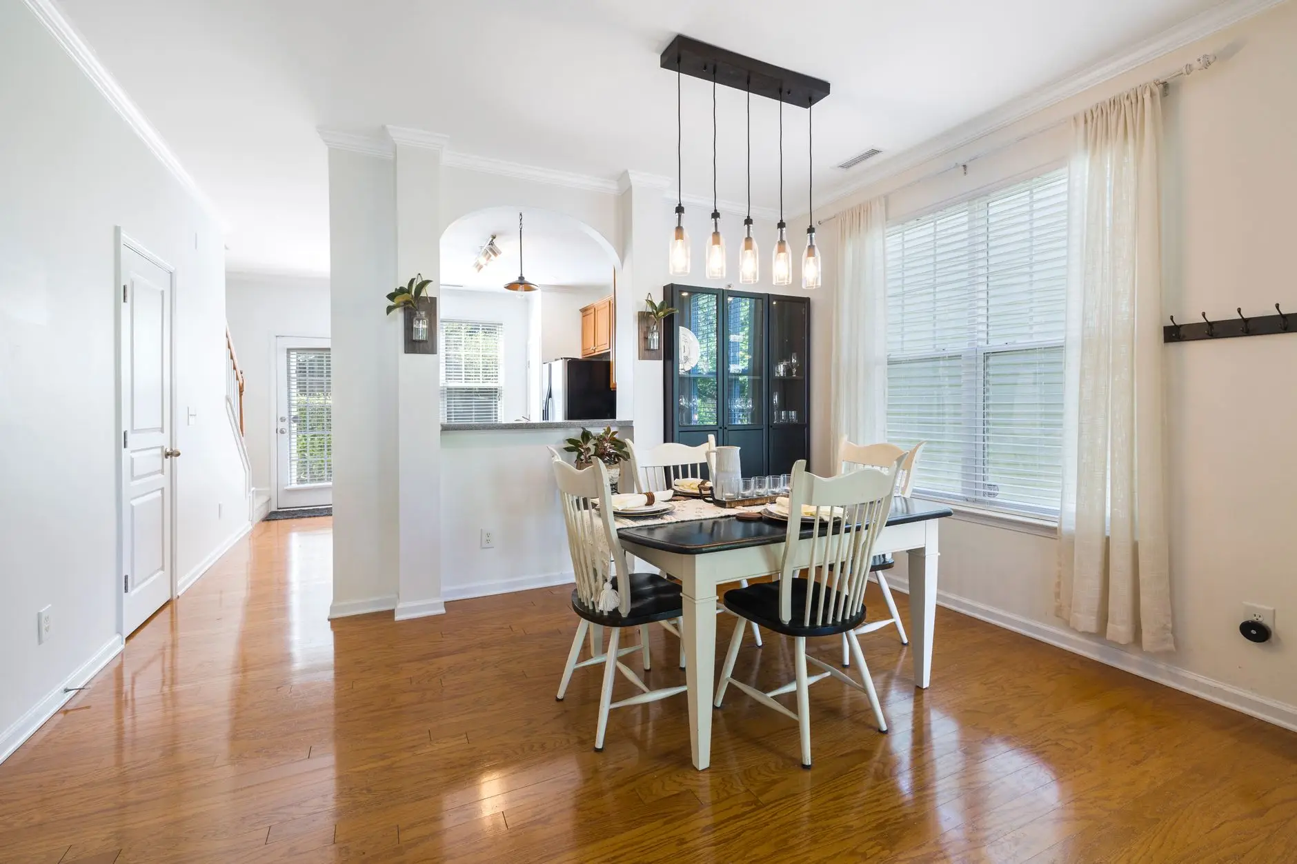 A five-bulb linear pendant light fixture hanging low over a farmhouse dining table