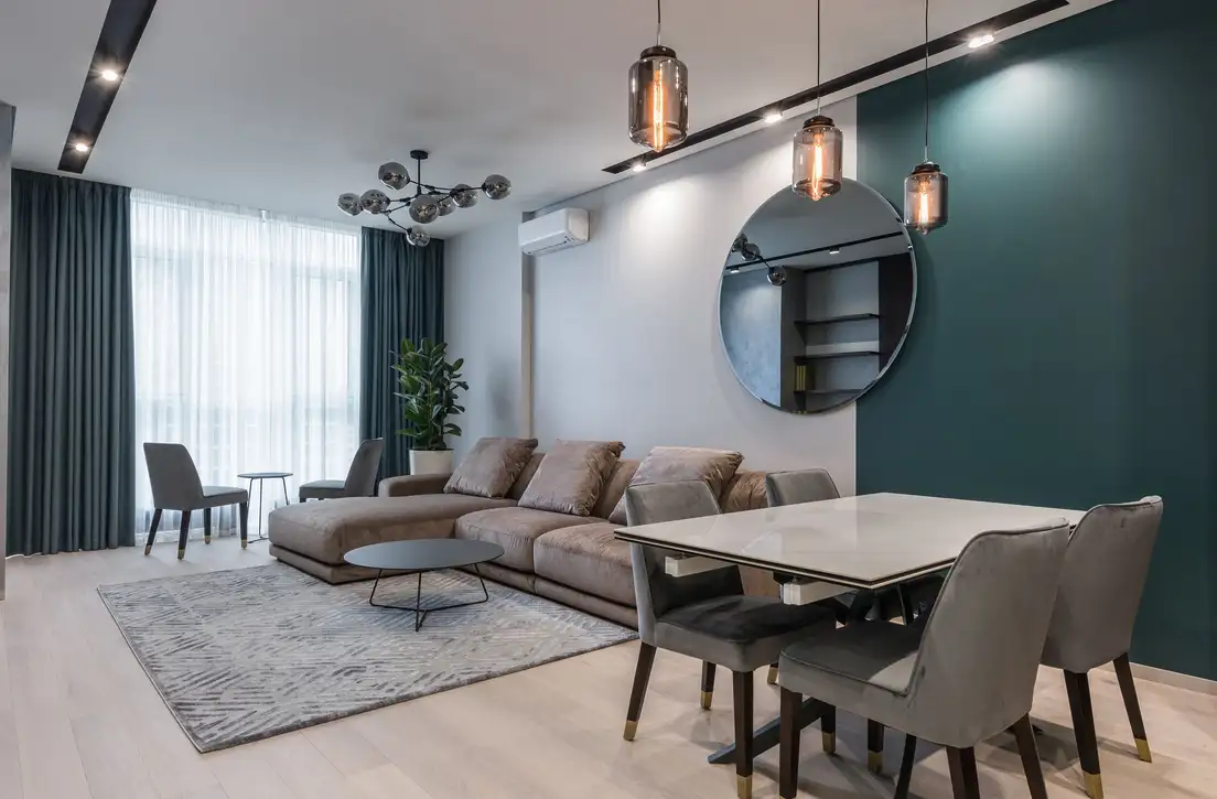 Three glass pendant lights hanging over a dining table beside a sectional sofa and rug, giving each zone its own lighting