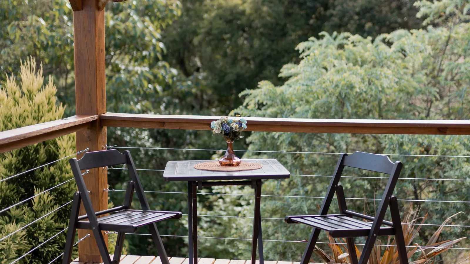 A small wooden pergola with string lights over a bistro table and two chairs on a patio